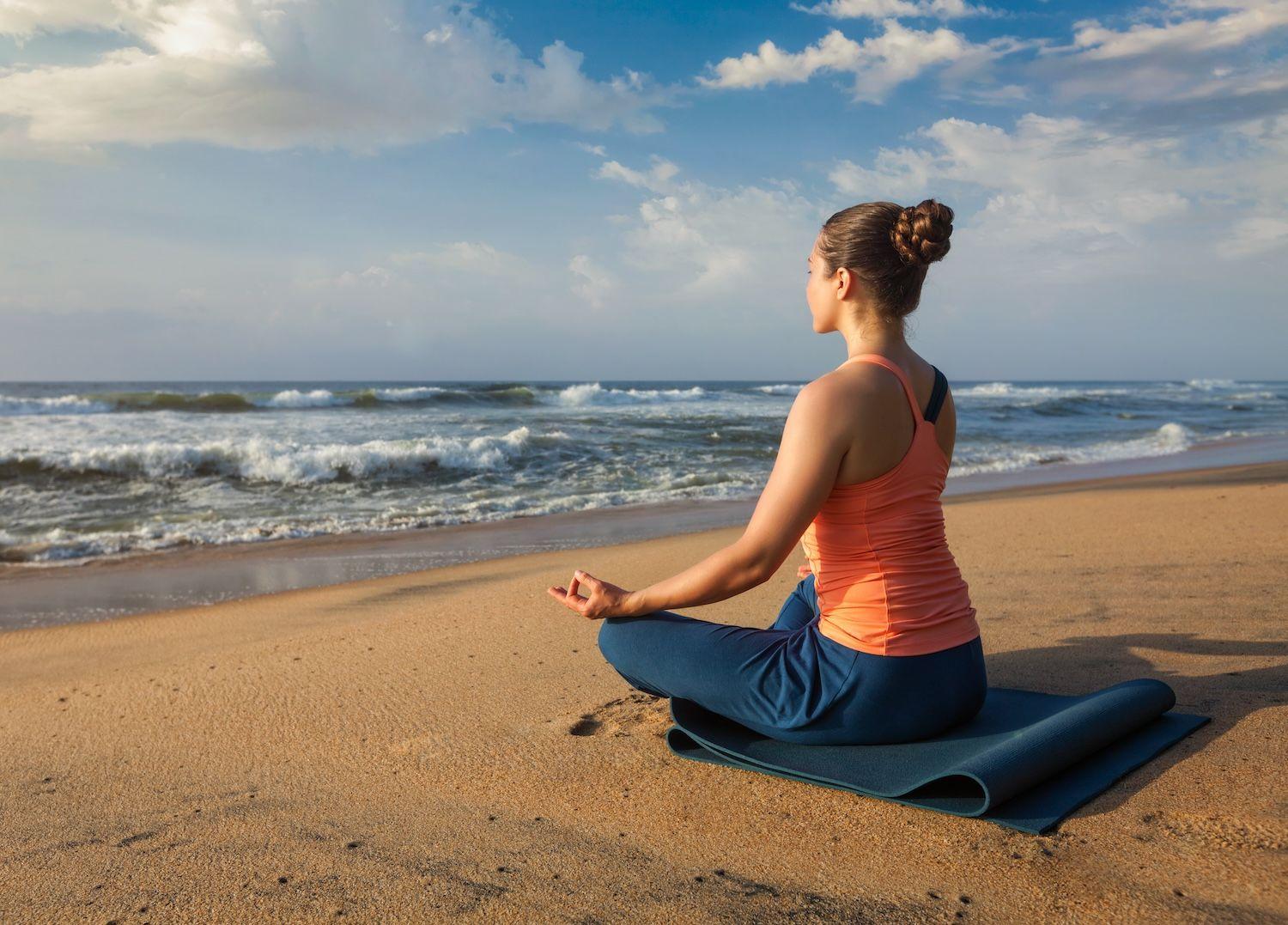 Woman sitting cross legged on beach looking toward ocean.