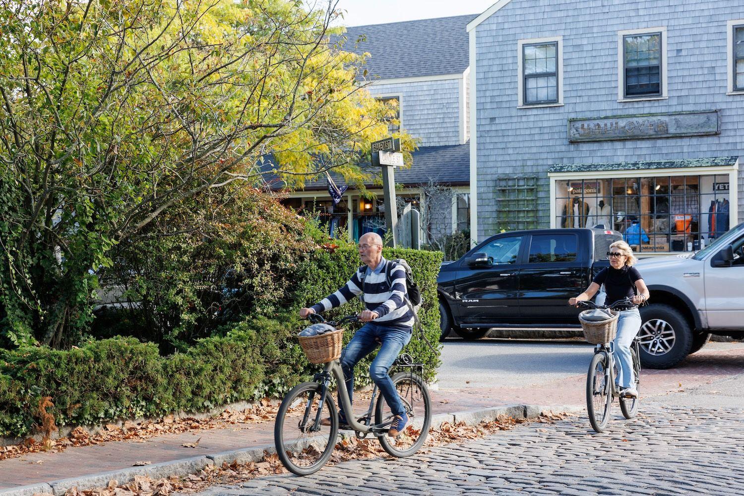 Couple biking on cobblestone street with stores in the background.