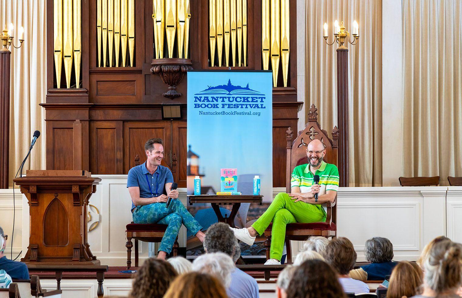 People facing two men talking on stage next to a sign reading Nantucket Book Festival.