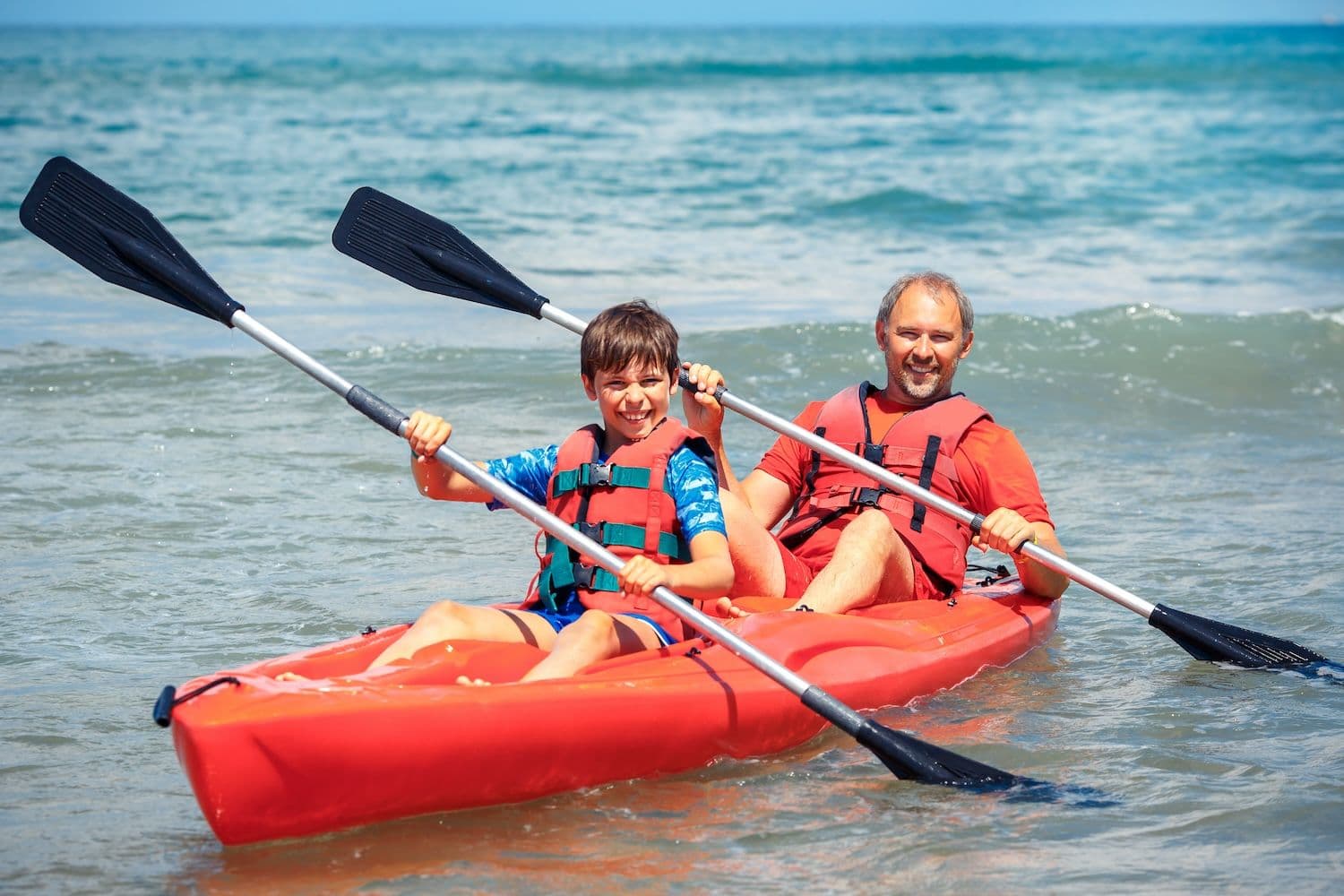 Father and son kayaking in calm waves.