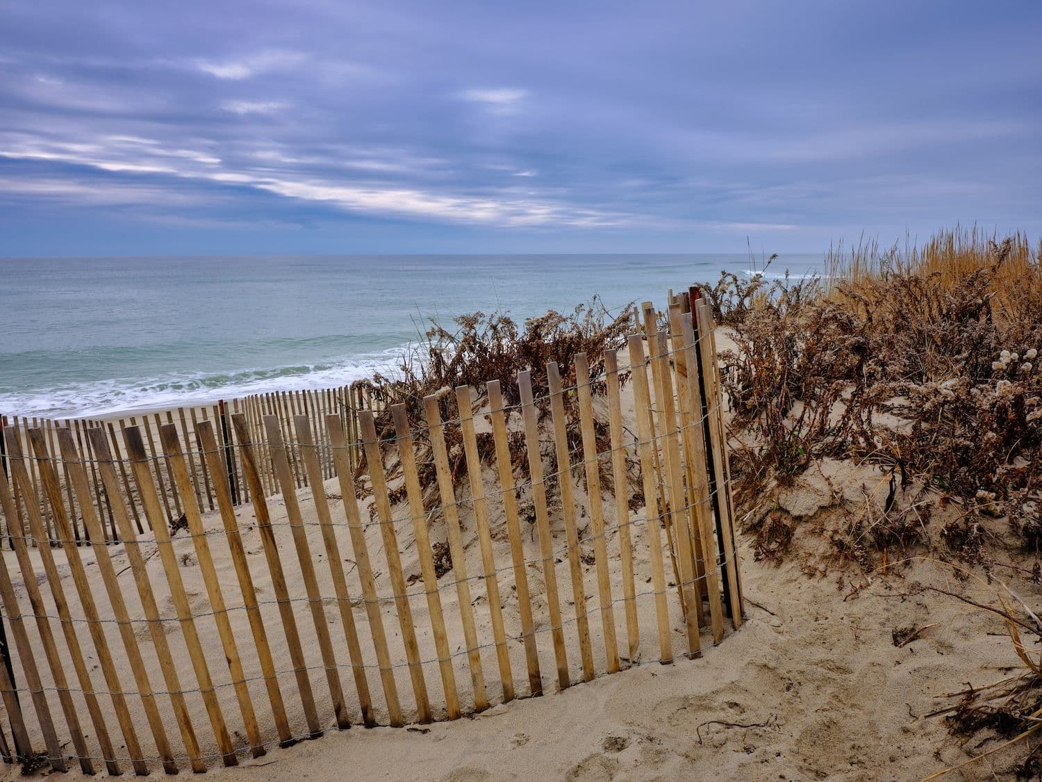 Nantucket beach with sand, brown dunes and clapboard fence.