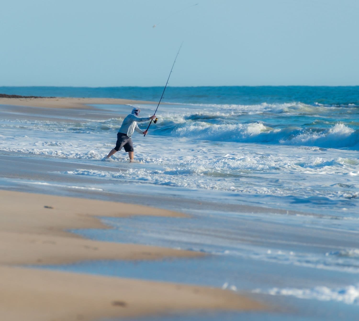 Man fishing on beach into ocean waves.